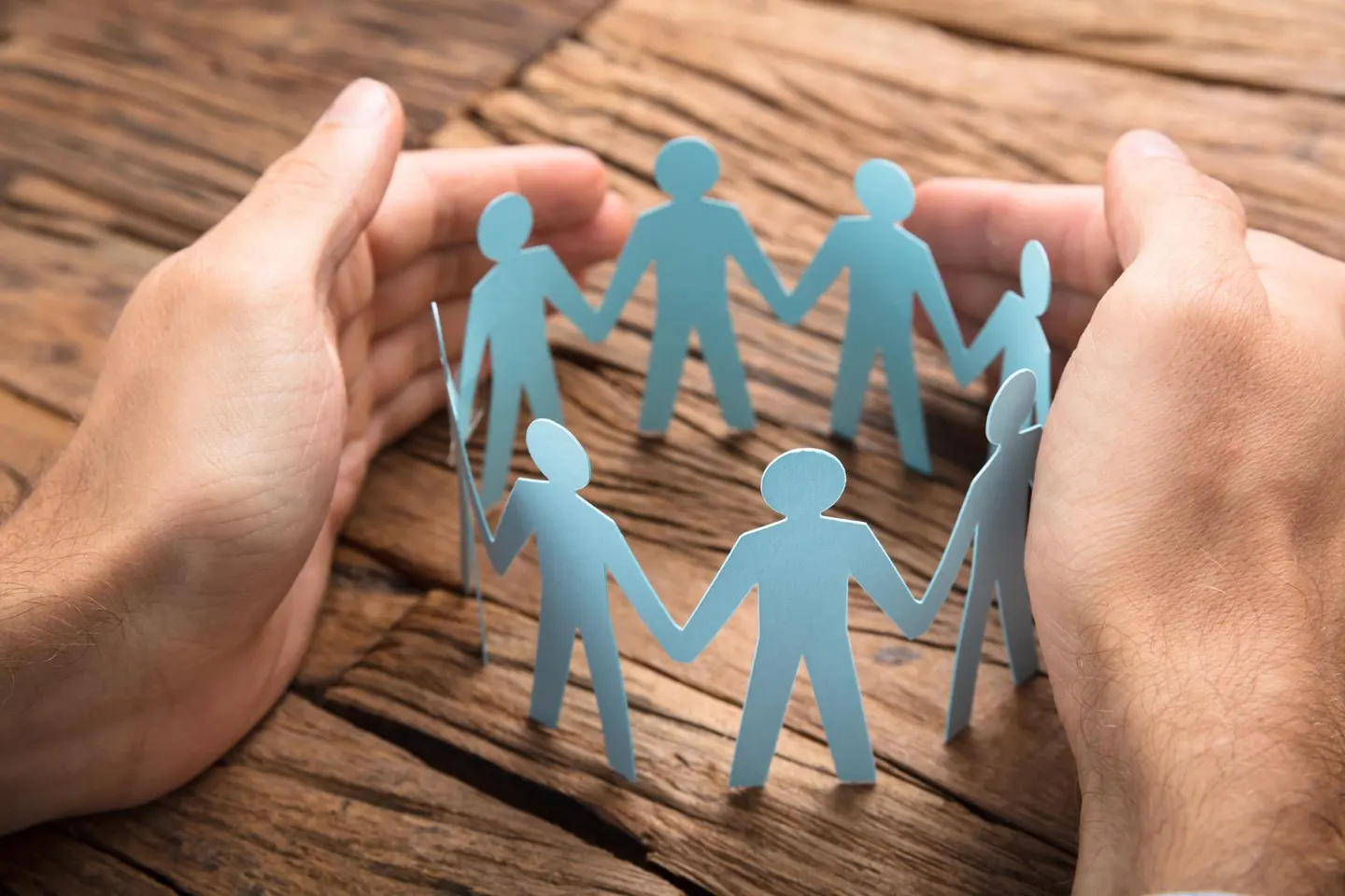 "photo of hands holding paper cutout of people holding hands in a circle