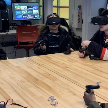 students wearing VR headsets sitting around a large square table in the Innovation Studio