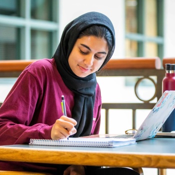 A woman writing in a notebook with computer open