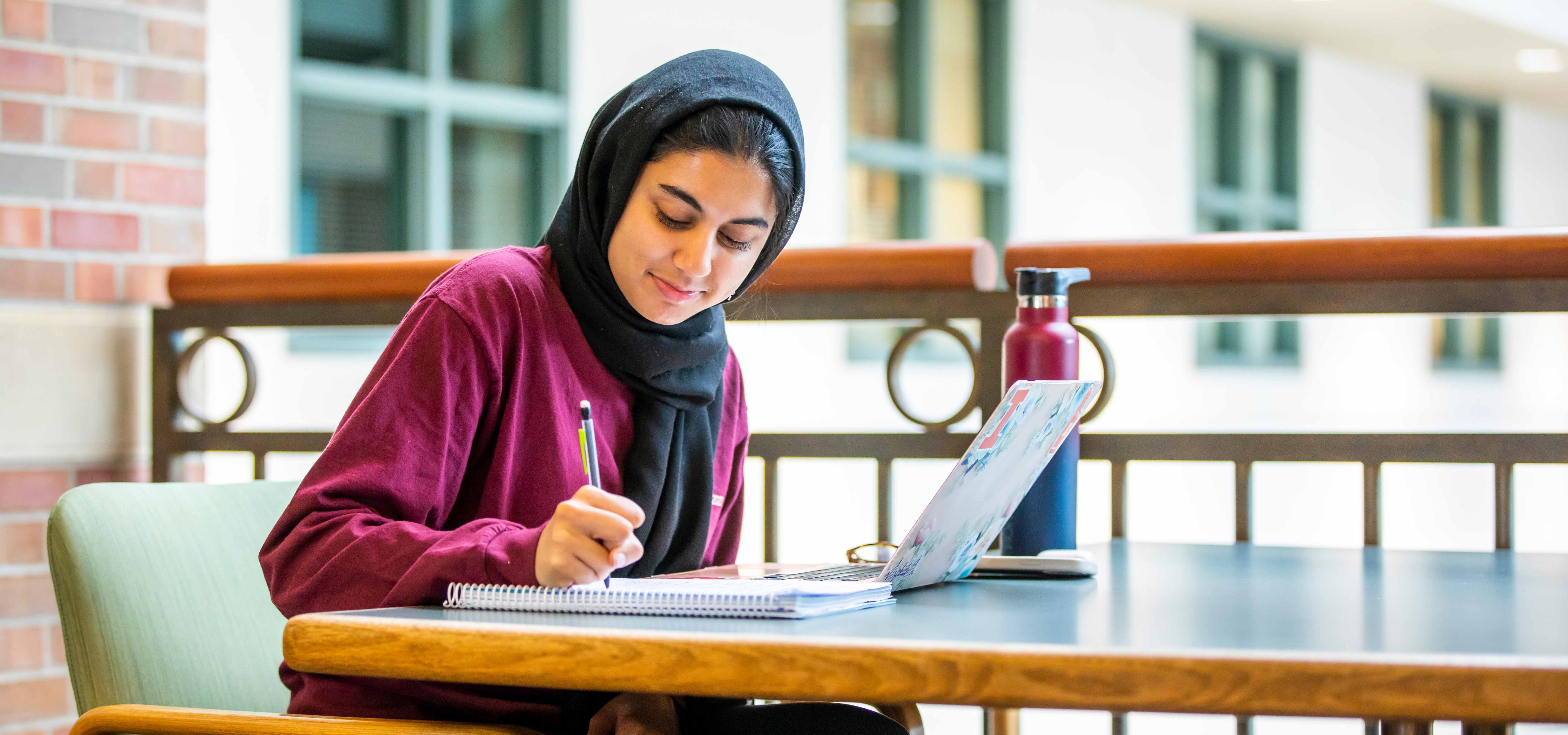 A woman writing in a notebook with computer open