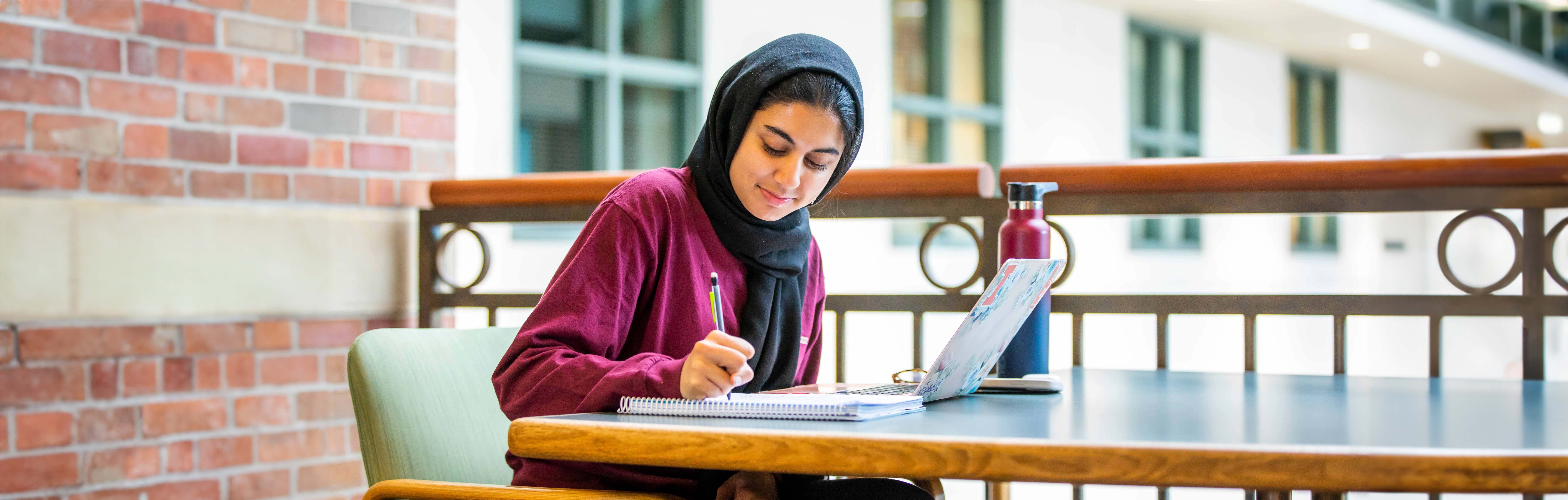 A woman writing in a notebook with computer open