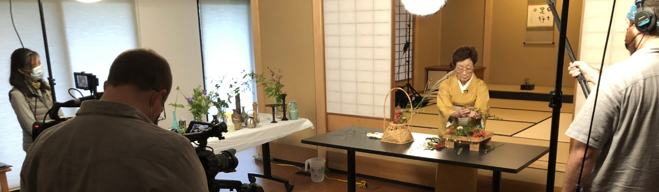 A woman in traditional japanese attire attends to a tea set while a film crew records her