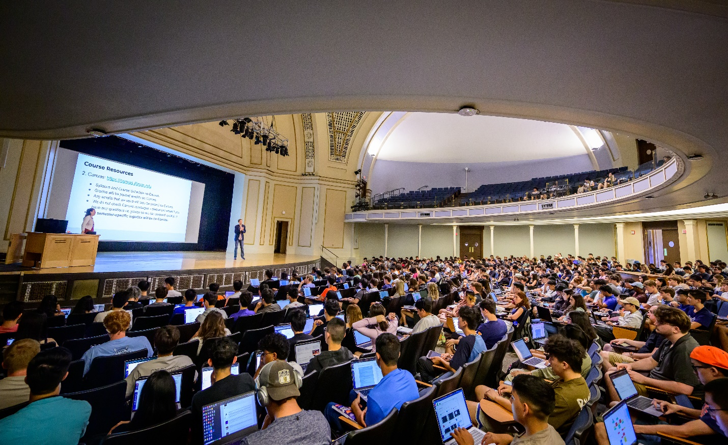 A professor lecturing in front of a large room of students