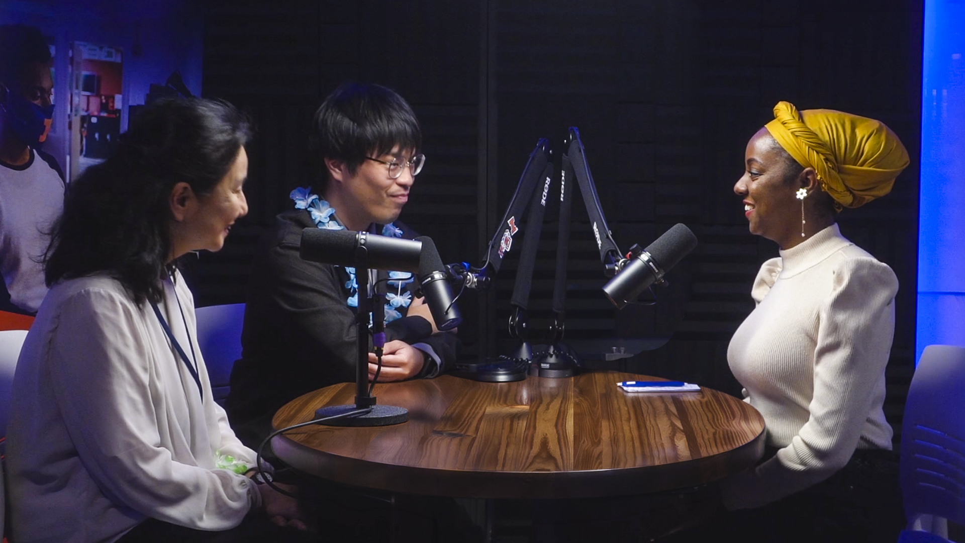 Photo of podcast guests sitting around a table with microphones in X3 Studio